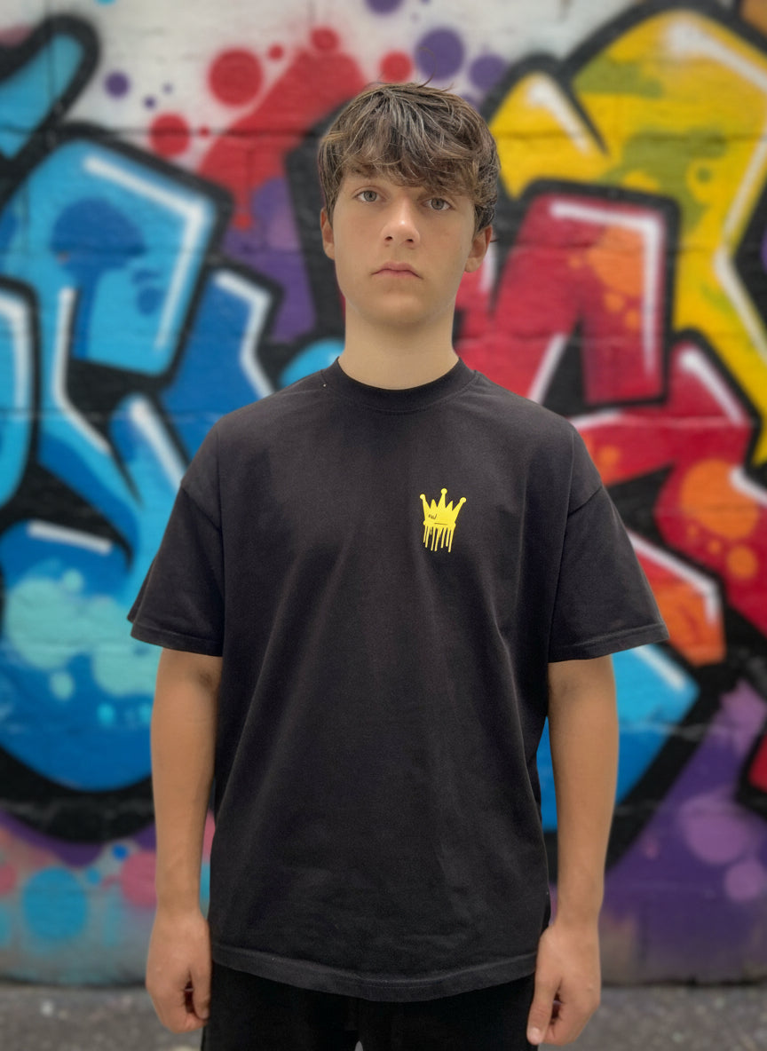 Person wearing a black t-shirt with a yellow logo on a plain background 2025 Trending Streetwear Grafitti